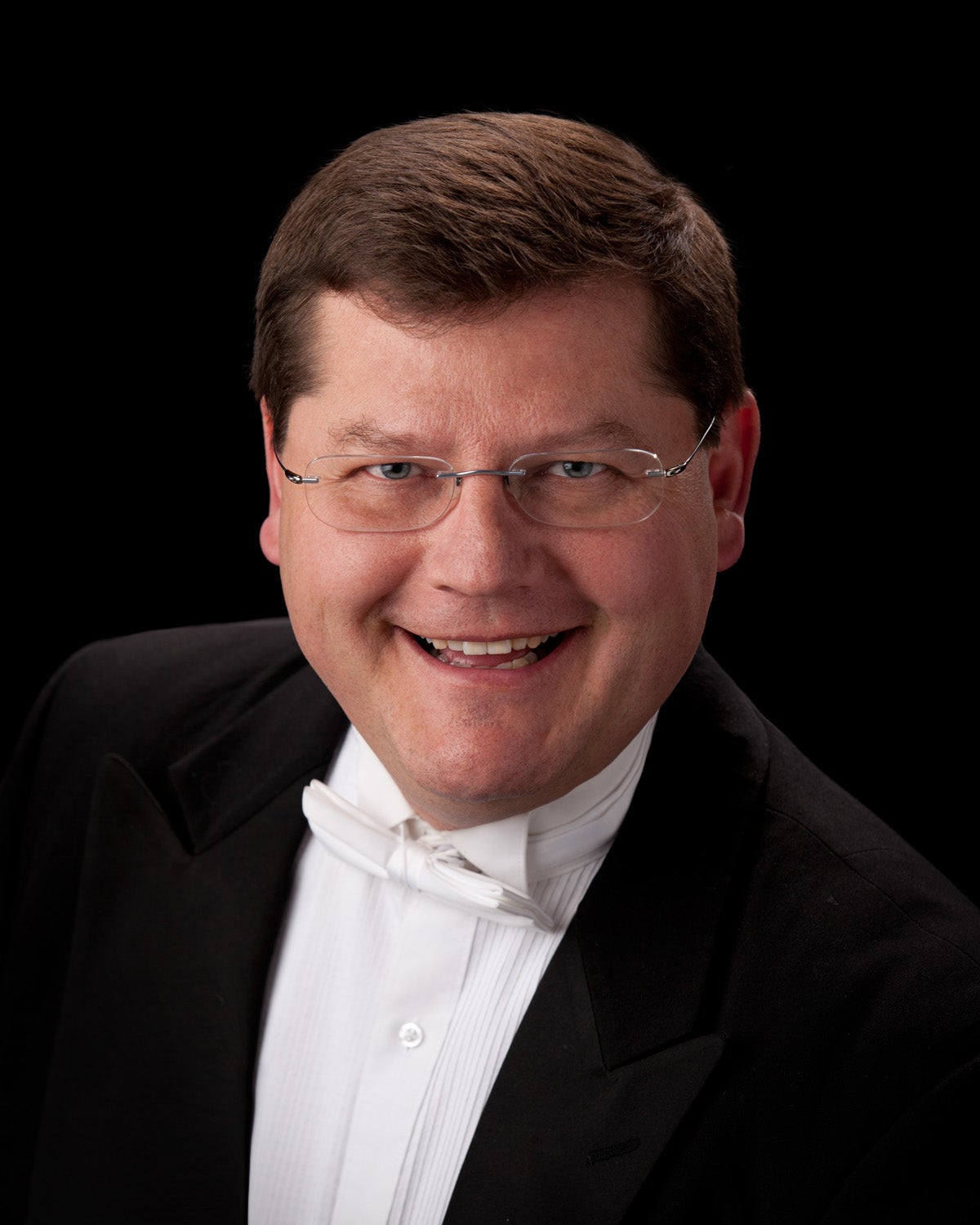 professional headshot of a choral conductor wearing a white bow tie, white shirt and black jacket
