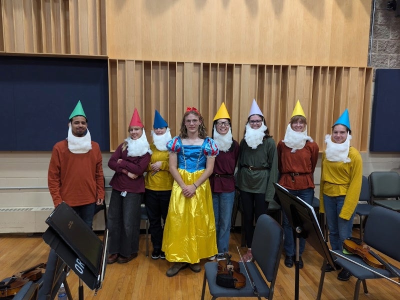 Standing in a line in a classroom, with violins lying on the chairs, the students line up in their dwarf and Snow White costumes. 
