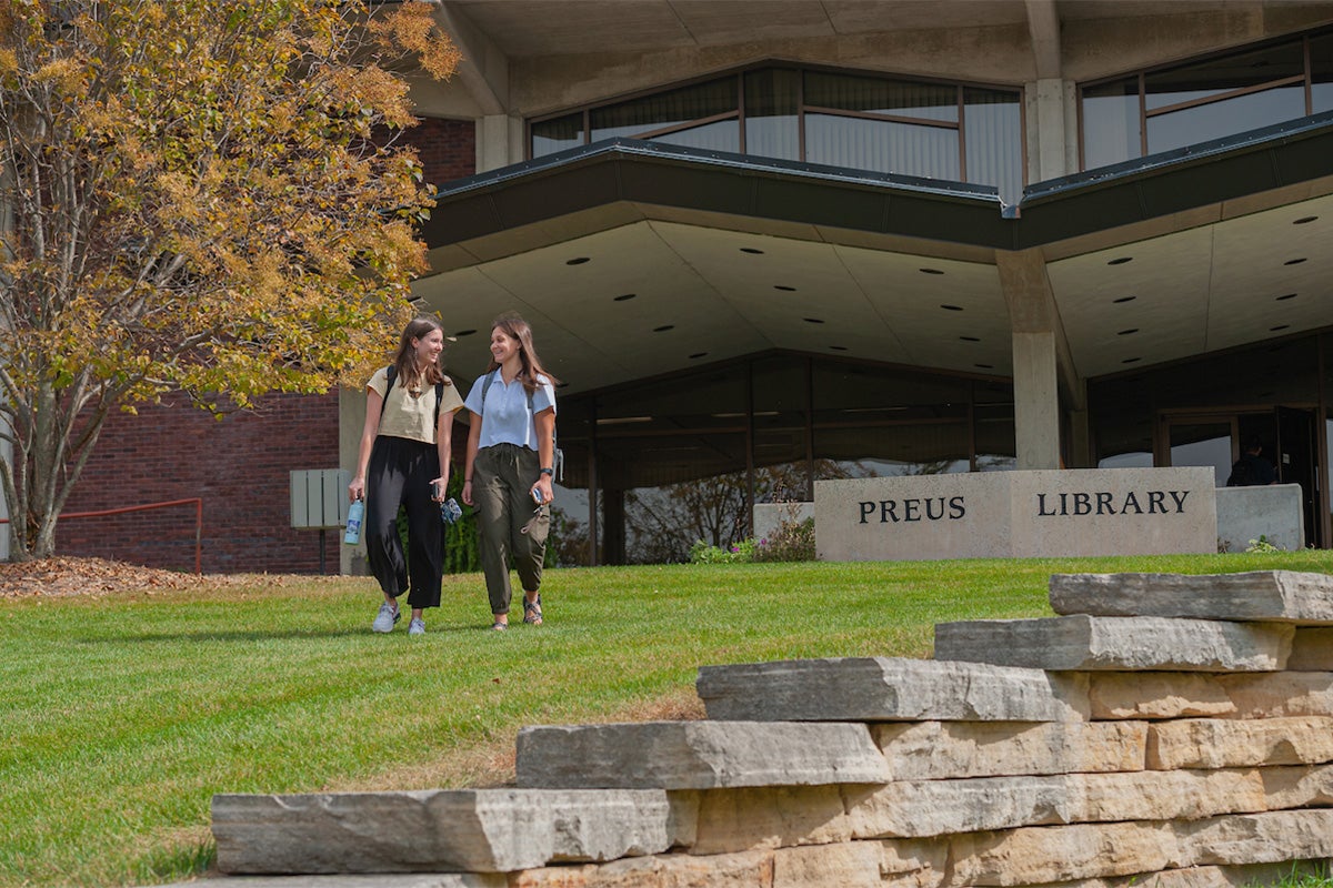 Two college students walk on the lawn in front of a library