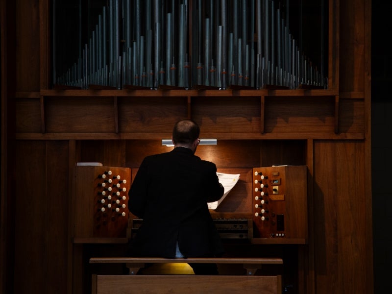 Alex Meszler seen from behind while playing an organ.