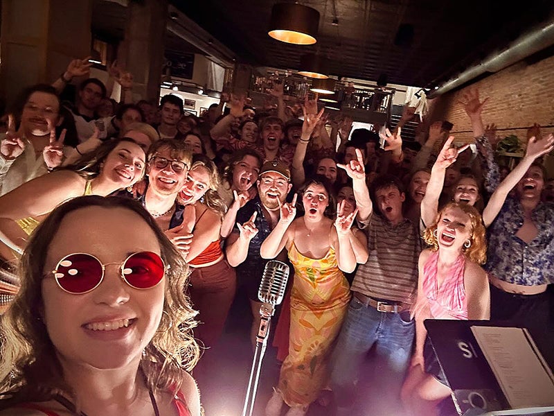 Woman takes a selfie from the stage with cheering crowd behind her.