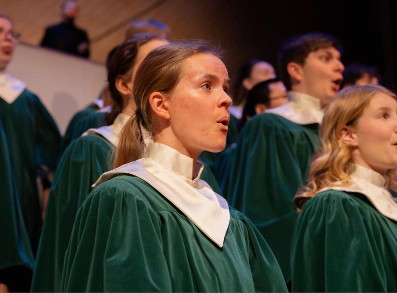 choir members singing, wearing green robes