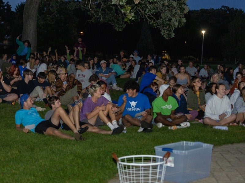 A bunch of students are sitting on a lawn at night.