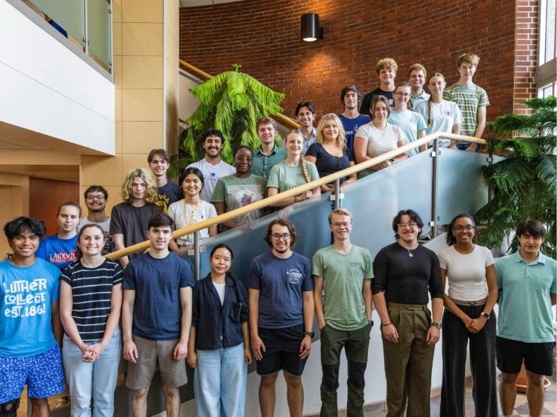 A large group of students pose for a picture in an atrium's stairway.