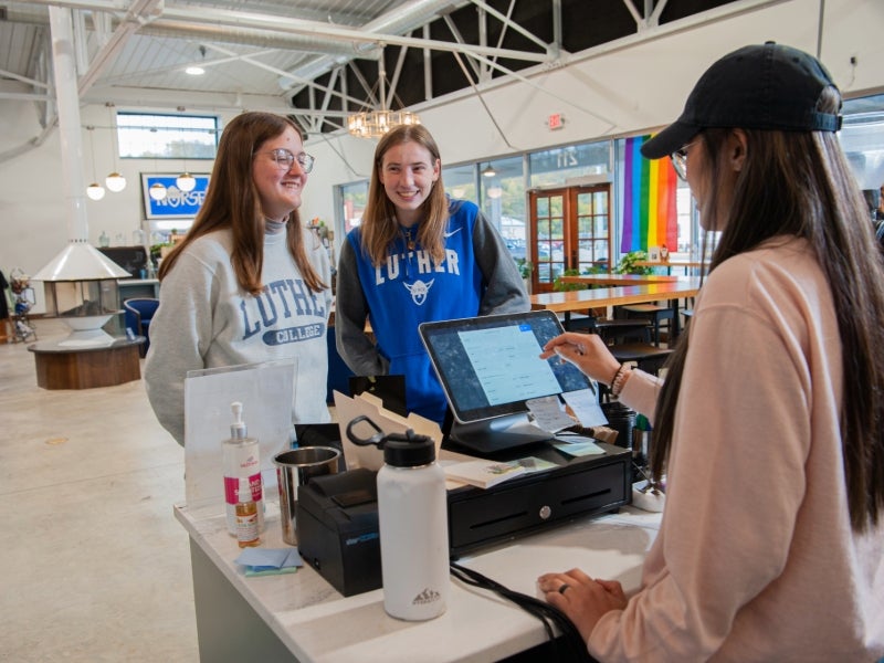 Two students wearing Luther gear place their orders from a barista in a large cafe with a high ceiling.