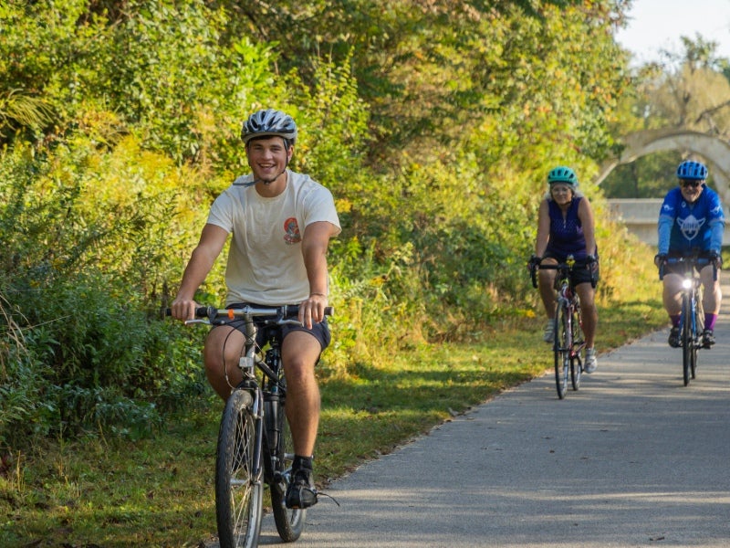 Three cyclists on a biking trail along a woodsy area.
