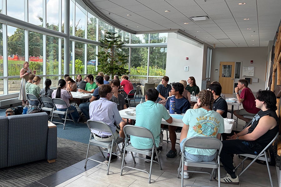 People sit at tables in an atrium with a wall of windows.
