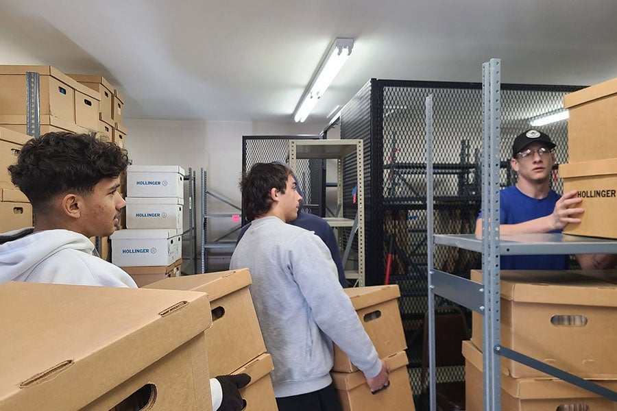 Three young men carrying boxes into a warehouse-type space