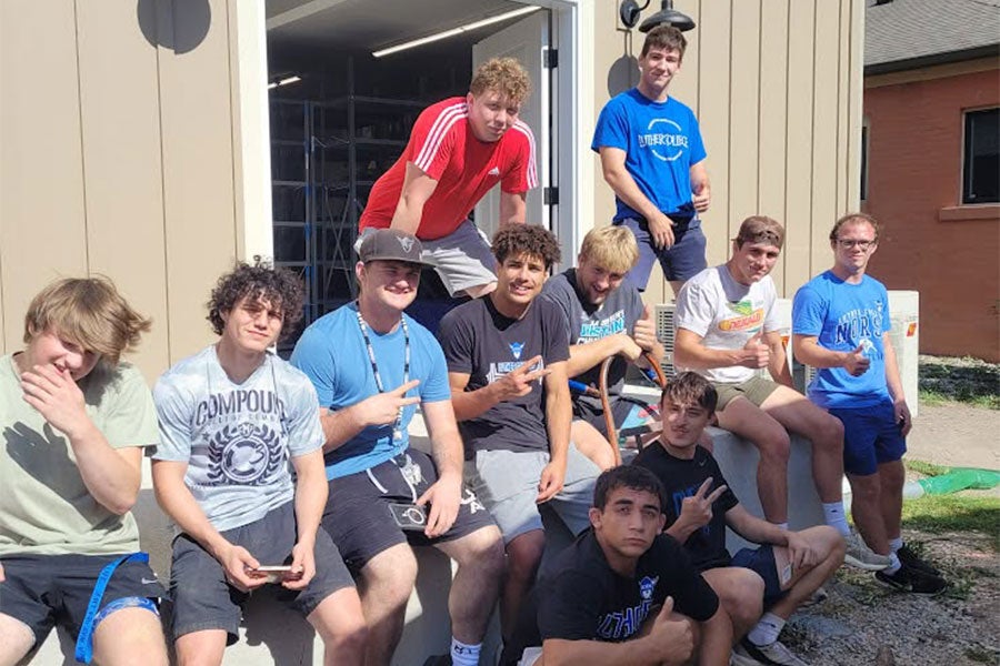 11 young men sit and stand outside a warehouse-type space