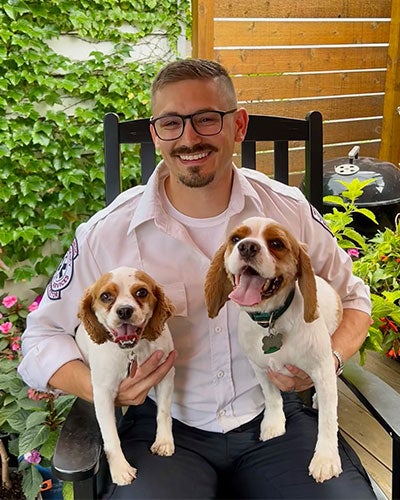 A man in a uniform sitting in a chair holding two dogs