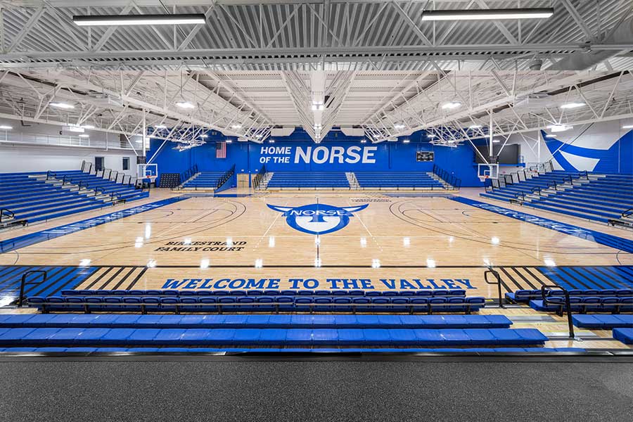 A sports court with a wood floor and blue bleacher seating on all sides of the court