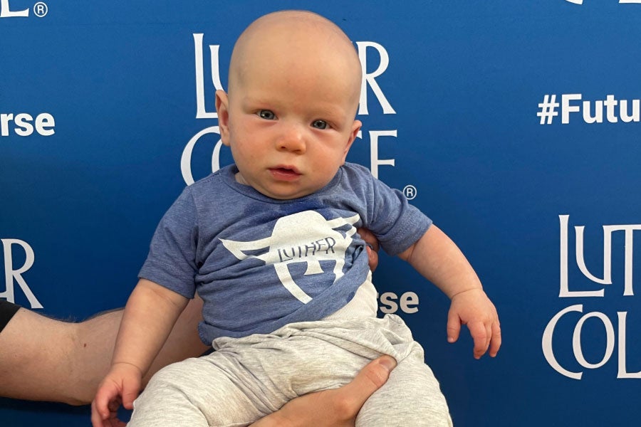 A baby in a Norse-head onesie being held in front of a blue backdrop