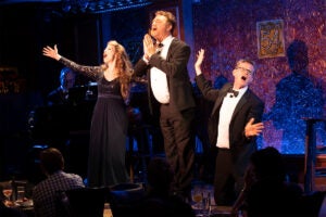 Three performers singing on a stage in New York City