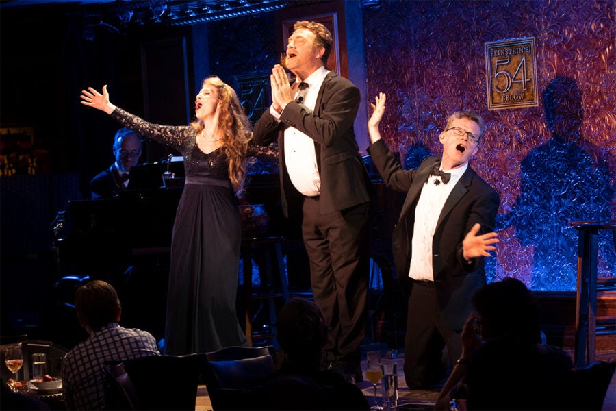 Three performers singing on a stage in New York City