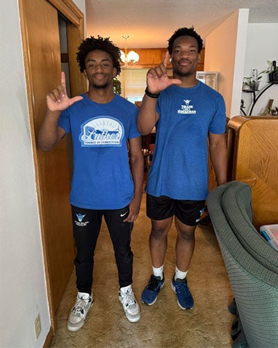 Two young men in blue shirts, each holding up one hand in an L shape
