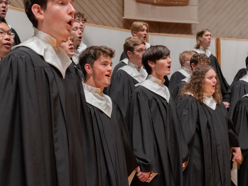 Choir members singing in their black robes with white collars