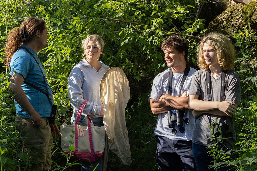 Four people with binoculars stand talking in lush foliage
