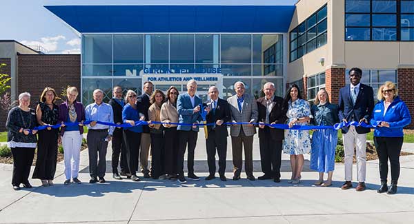 17 people hold a long blue ribbon in front of a building