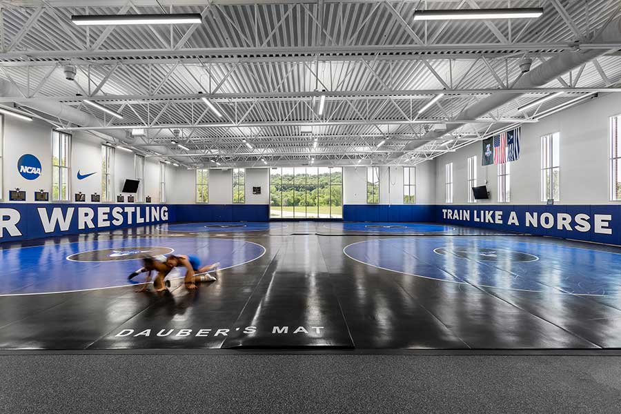 A large room with a giant window, several wrestling mats, and two wrestlers