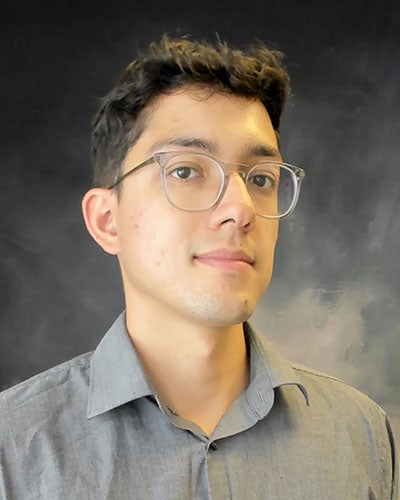 A head shot of a man in glasses in front of a gray backdrop