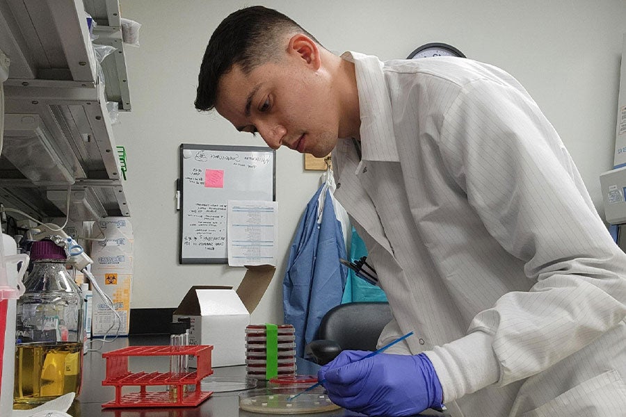 A man in a white lab coat seen in profile working with materials at a lab bench