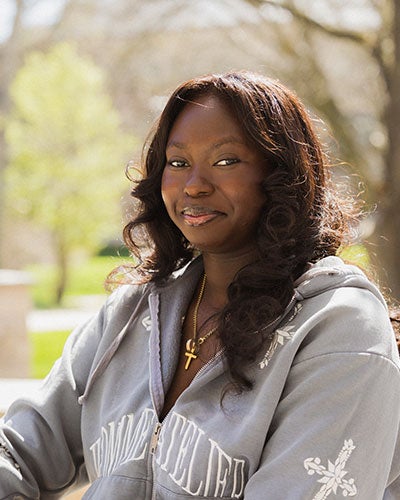 A smiling woman in the sunlight with trees in the background