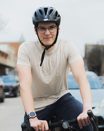 A young man in a bike helmet and a white T-shirt riding a bicycle