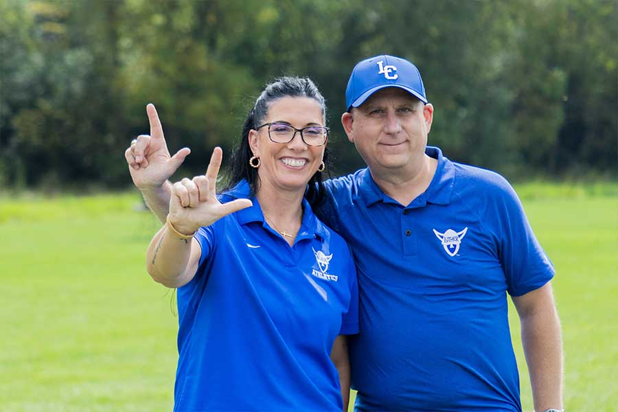 A woman and man dressed in blue making an L shape with their hands
