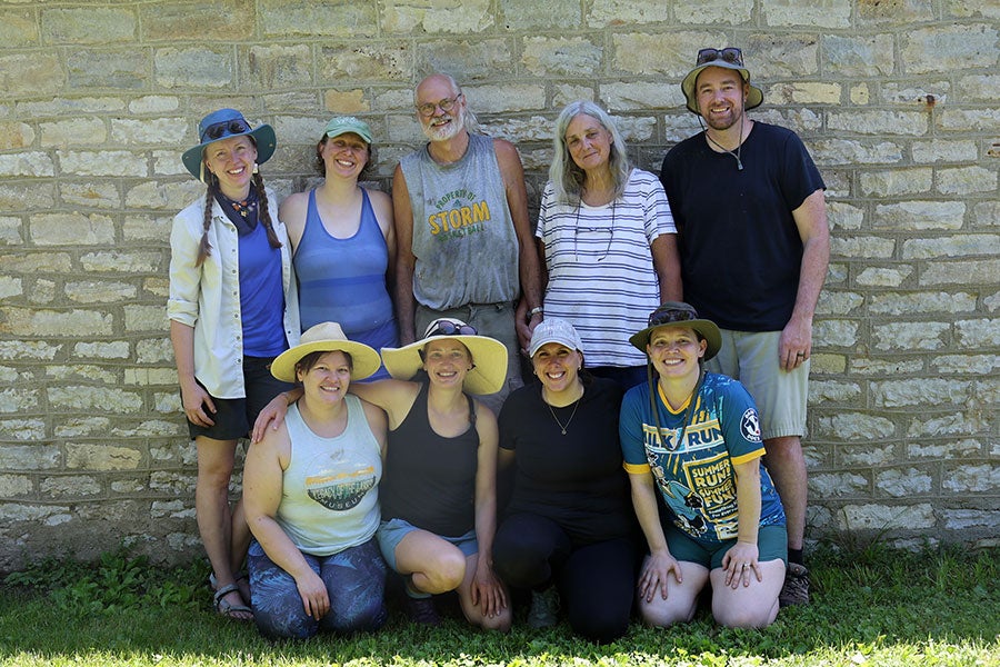 A group of nine people posing in front of a stone wall