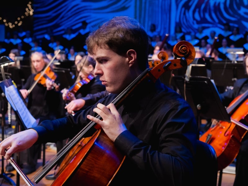 an orchestra plays, with a cellist in the foreground