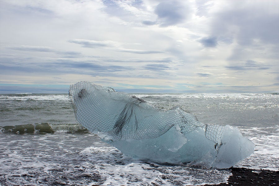 A large chunk of ice draped with a delicate piece of net on a seashore