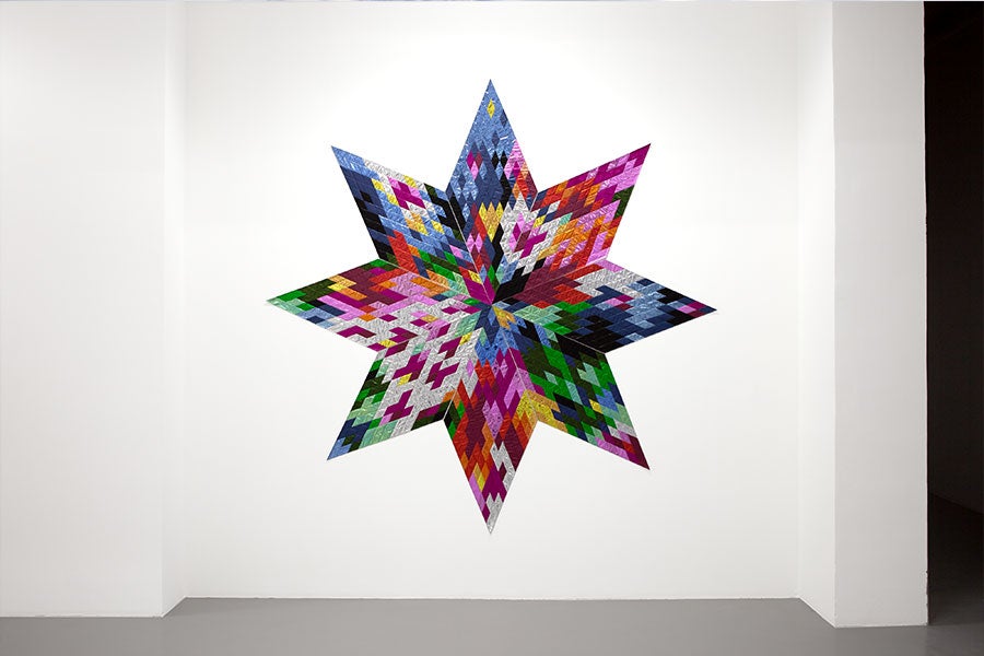 A star-shaped quilt made from shiny multicolored mylar hangs on a white gallery wall