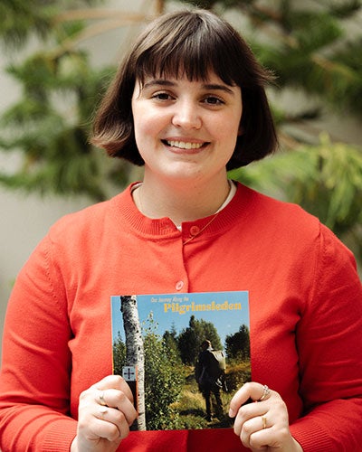 A young woman in a reddish cardigan holding up a book