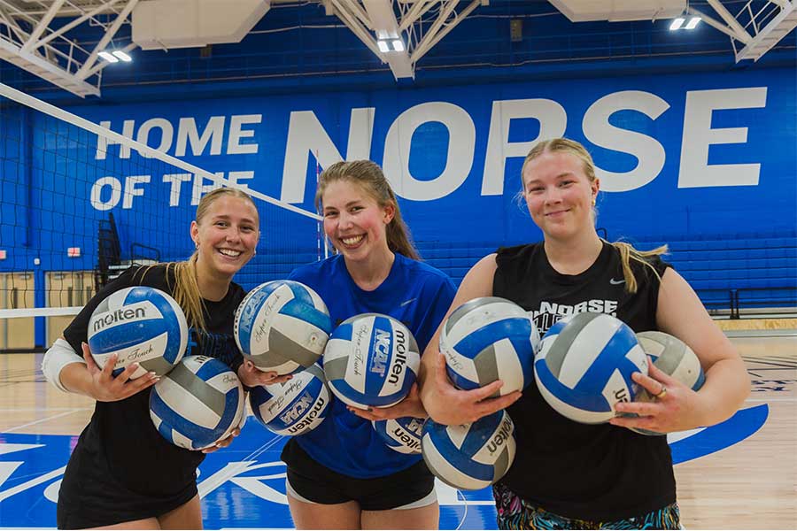 Three women holding volleyballs on a volleyball court