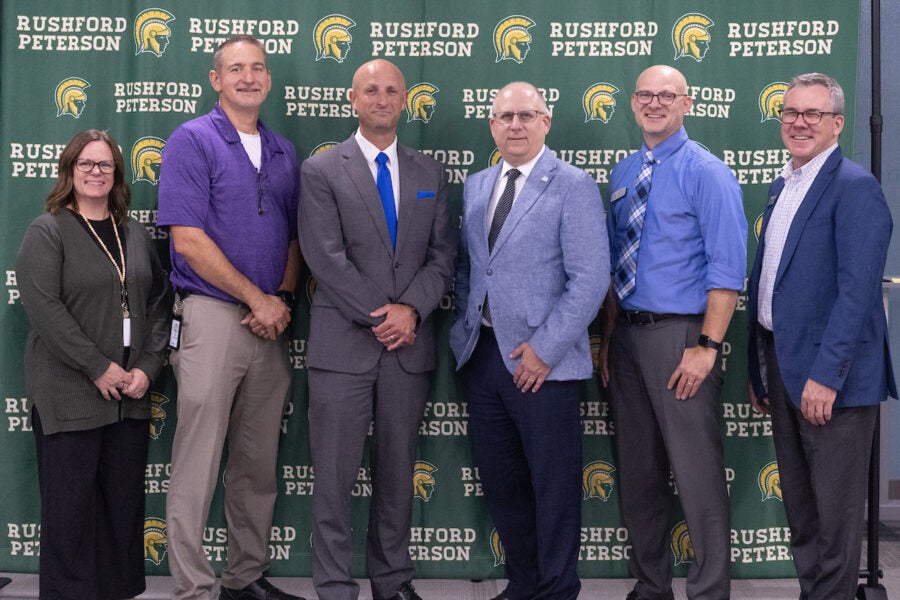 six people stand in front of a Rushford-Peterson School backdrop