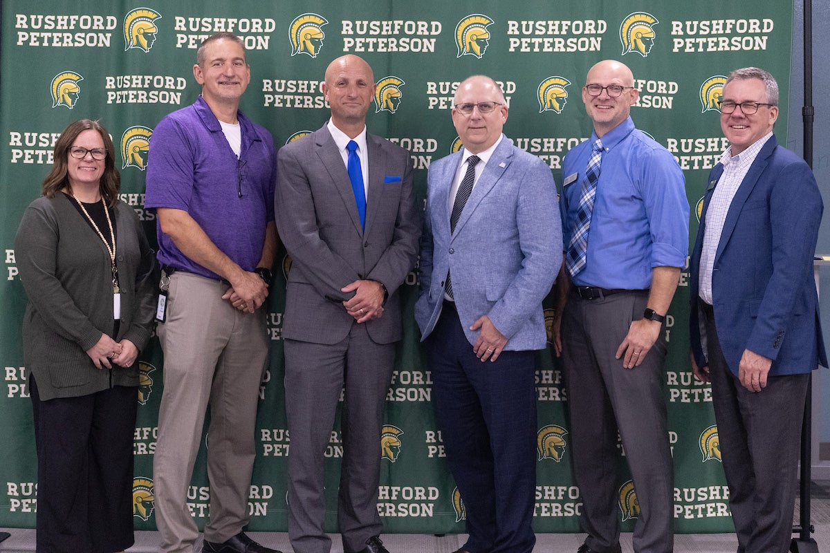 six people stand in front of a Rushford-Peterson School backdrop