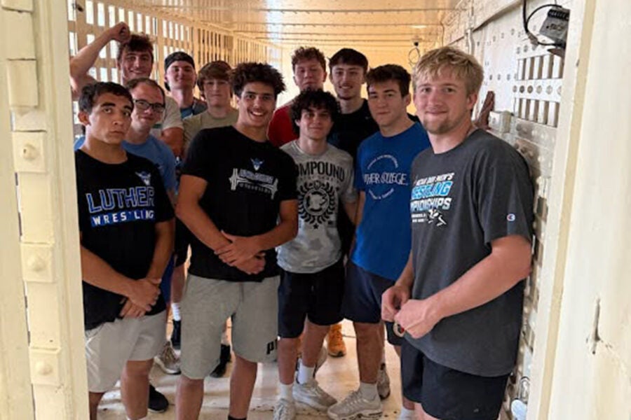 a group of young men wearing Luther wrestling t-shirts pose in a basement space