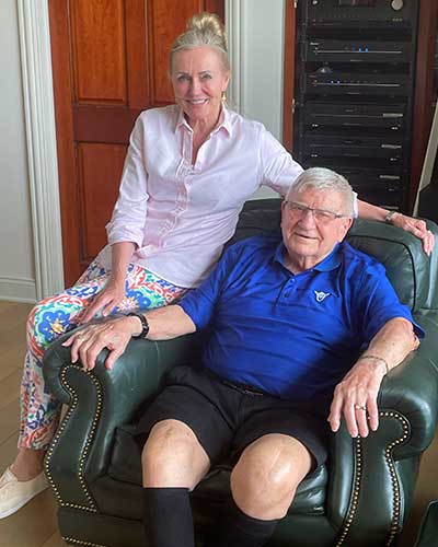 An older man sitting on an easy chair with a woman sitting next to him on the arm of the chair