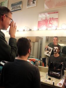 Theater student wearing animal makeup and professor commenting on it.
