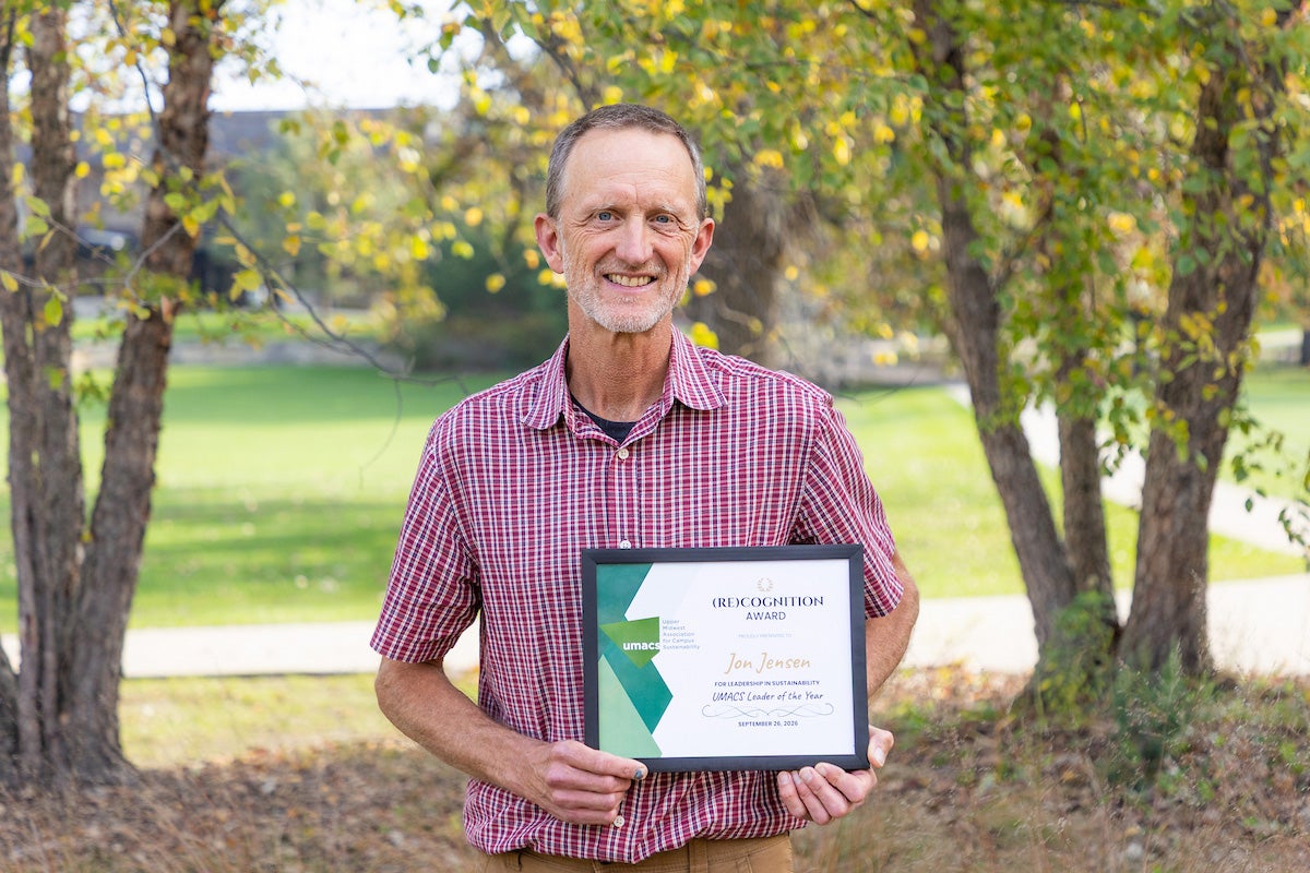 Jon Jensen holds an award certificate while standing outside at Bentdahl Commons at Luther College.