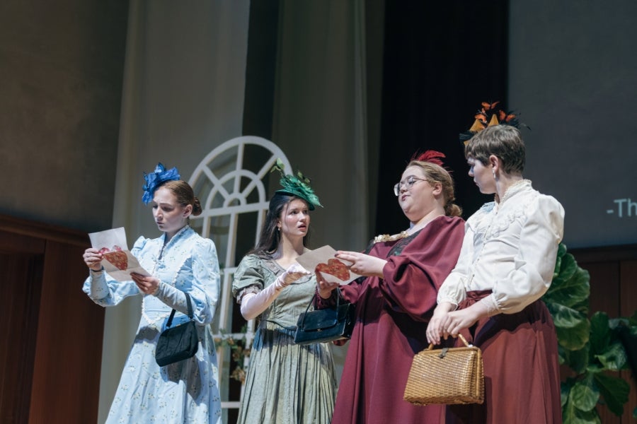 Four female performers on stage wearing fancy dresses and hats