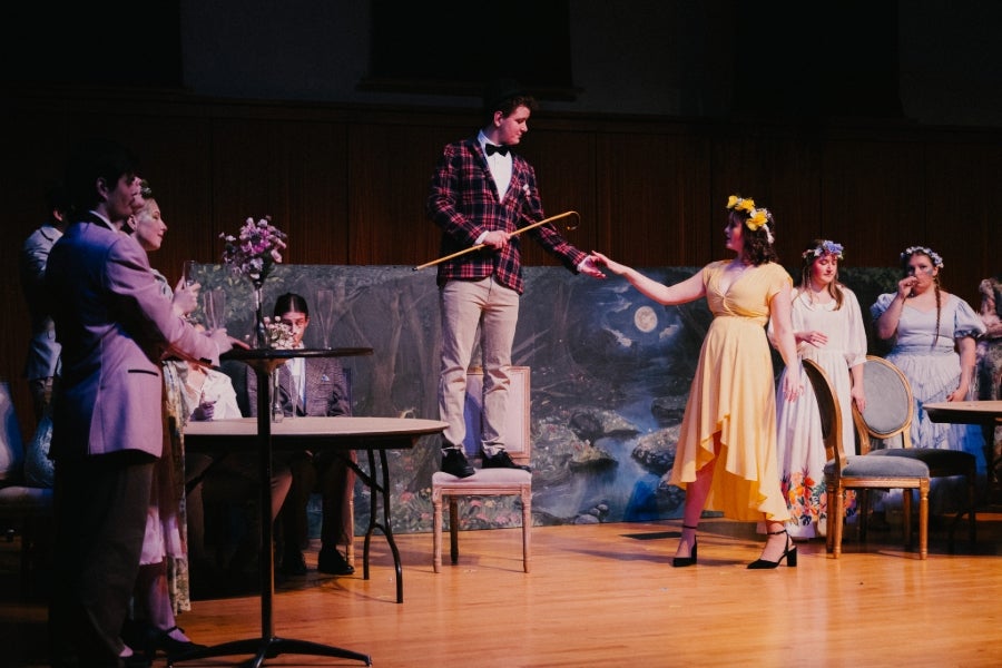 A male and female singer stand at center stage, holding hands, surrounded by other singers